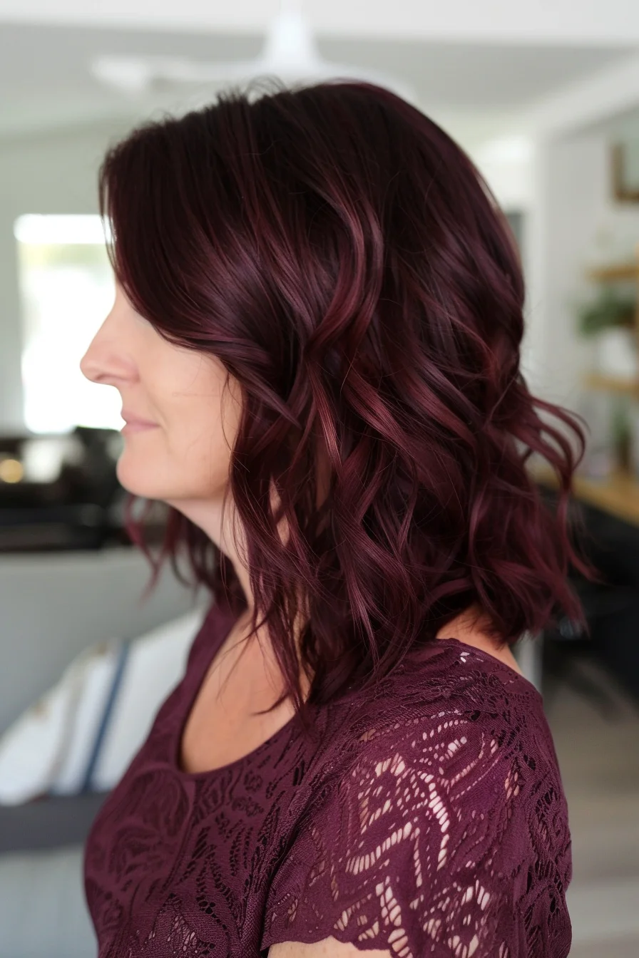 Long, layered waves colored in deep mulberry reveal stunning movement and depth. Darker roots transition flawlessly into brighter wine-toned lengths, while subtle burgundy highlights catch light beautifully. Soft waves styled with purposeful texture show off the remarkable dimension of these rich, berry-inspired shades.