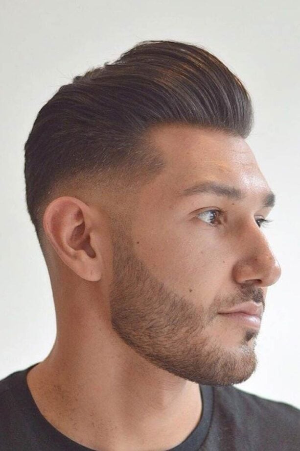 Man with voluminous hairstyle, trimmed beard, black shirt.