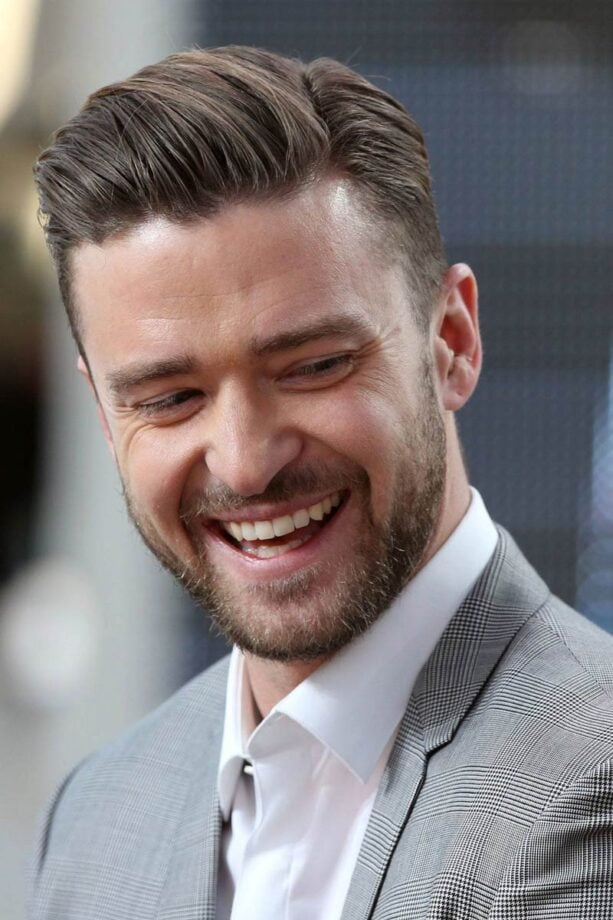 Man in gray suit smiling, blurred background.