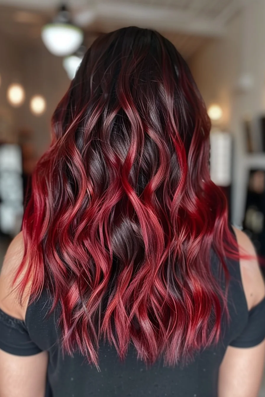 Dramatic noir base melts seamlessly into vibrant cherry-red pieces that cascade through flowing waves. The bold contrast between dark roots and vivid red creates an eye-catching gradient effect, while long layers cut at varying lengths allow the colors to blend naturally. Bright crimson highlights peek through darker sections, adding stunning dimension throughout.