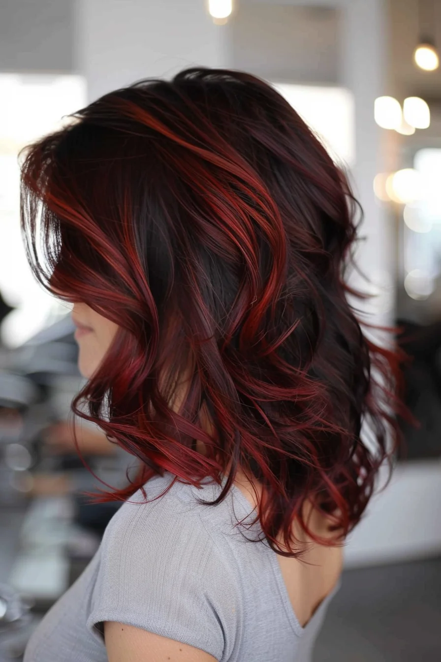 Vibrant red highlights weave through dark chocolate base color in a bold display of dimensional coloring. Medium-length layers styled with gentle waves showcase the beautiful blend of shades, while bright pieces frame the face. The painted technique creates natural-looking movement throughout.