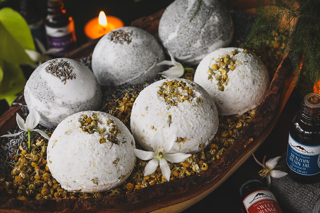 Homemade bath bombs surround by chamomile flowers and candles. 