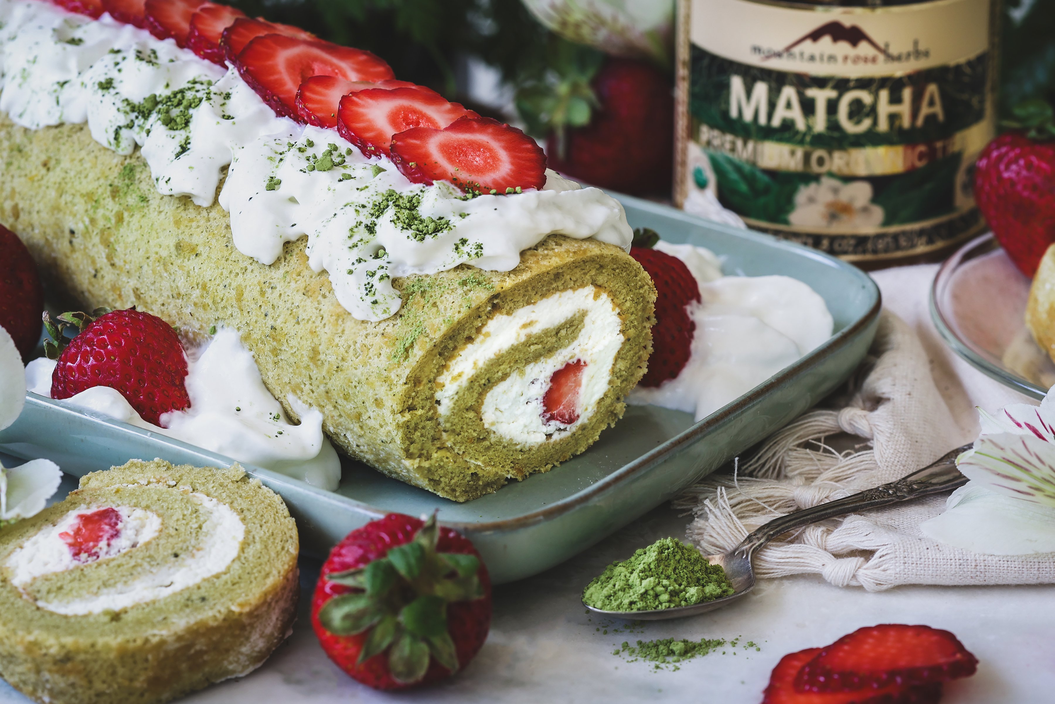 Strawberry matcha swiss roll log topped with fresh strawberries and whipped cream.